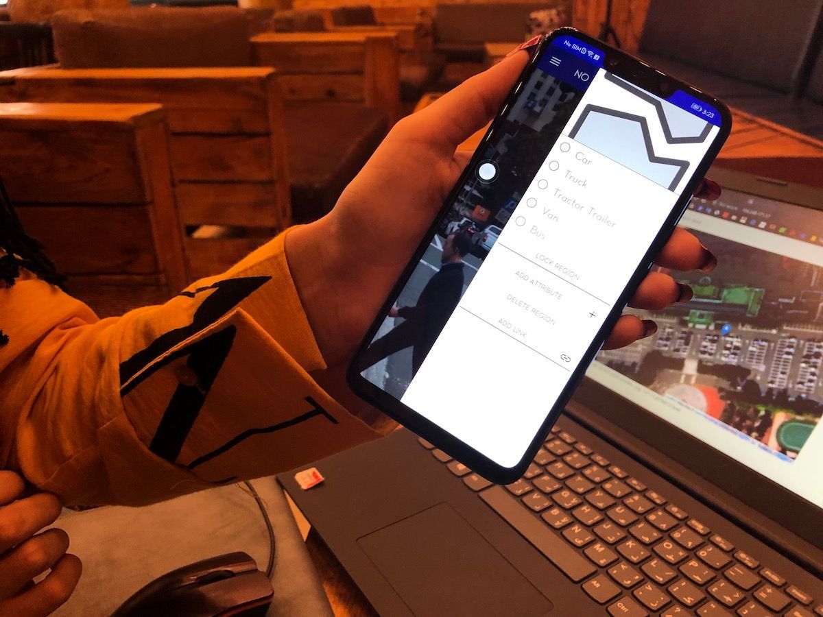 a person holding a mobile phone with a laptop in background