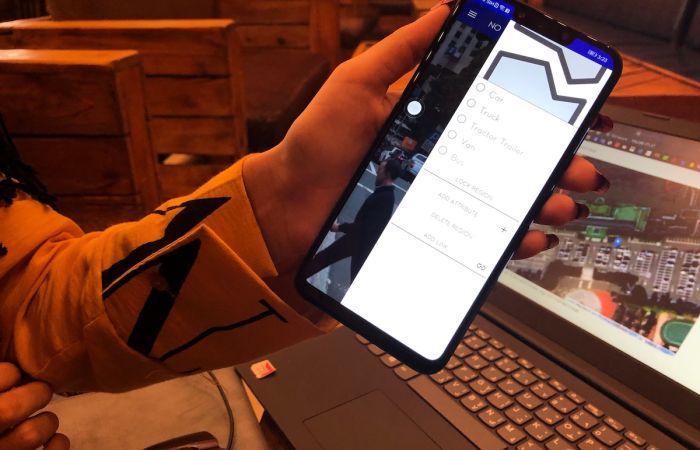 a person holding a mobile phone with a laptop in background